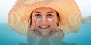 donna con cappello di paglia che applica crema solare viso estate 2025