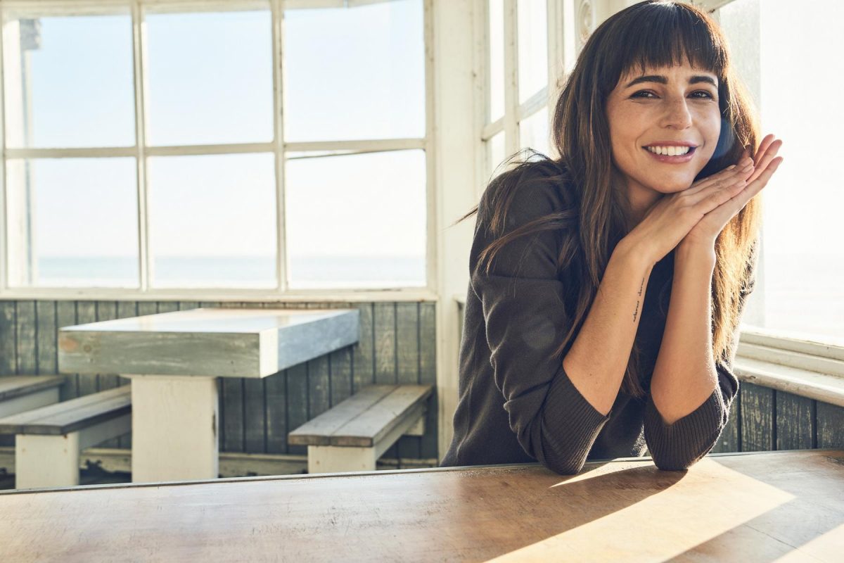Modella con maglia girocollo scura Dockers, appoggiata a un tavolo accanto alle finestre