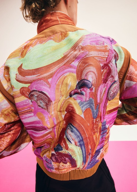 Retro del blouson A-POC ABLE ISSEY MIYAKE x Etsu Egami, con un ritratto jacquard nei toni arancio, rosa e verde chiaro.