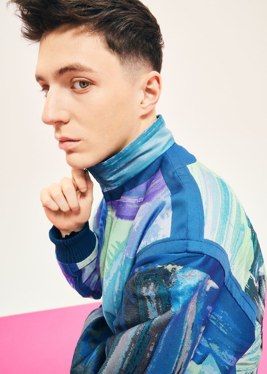 Dettaglio della giacca Issey Miyake x Etsu Egami indossata, con collo alto e tessuto jacquard blu, verde e viola.