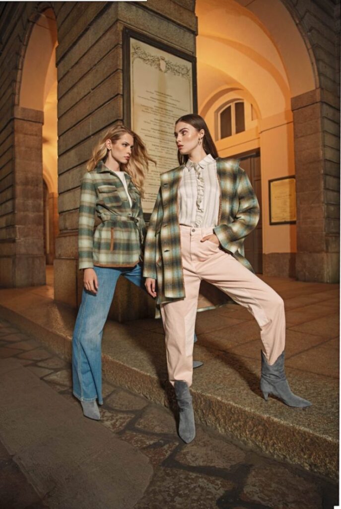 Due modelle con capispalla a quadri, jeans e pantaloni rosa sotto un porticato illuminato a Milano