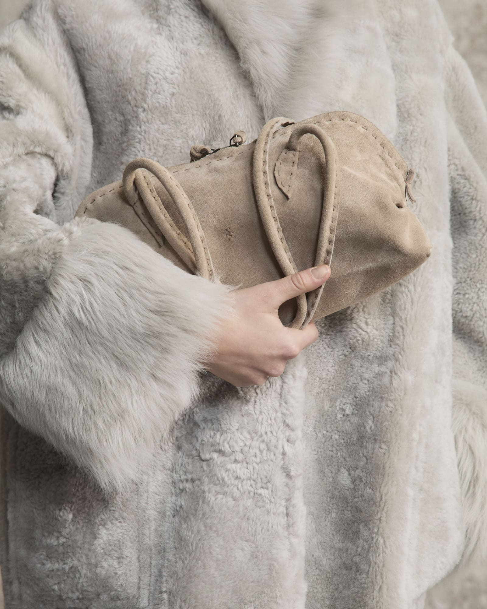 Borsa Henry Beguelin Bolla Bassa beige tenuta tra le mani, con manici morbidi, cuciture visibili e omino ricamato.