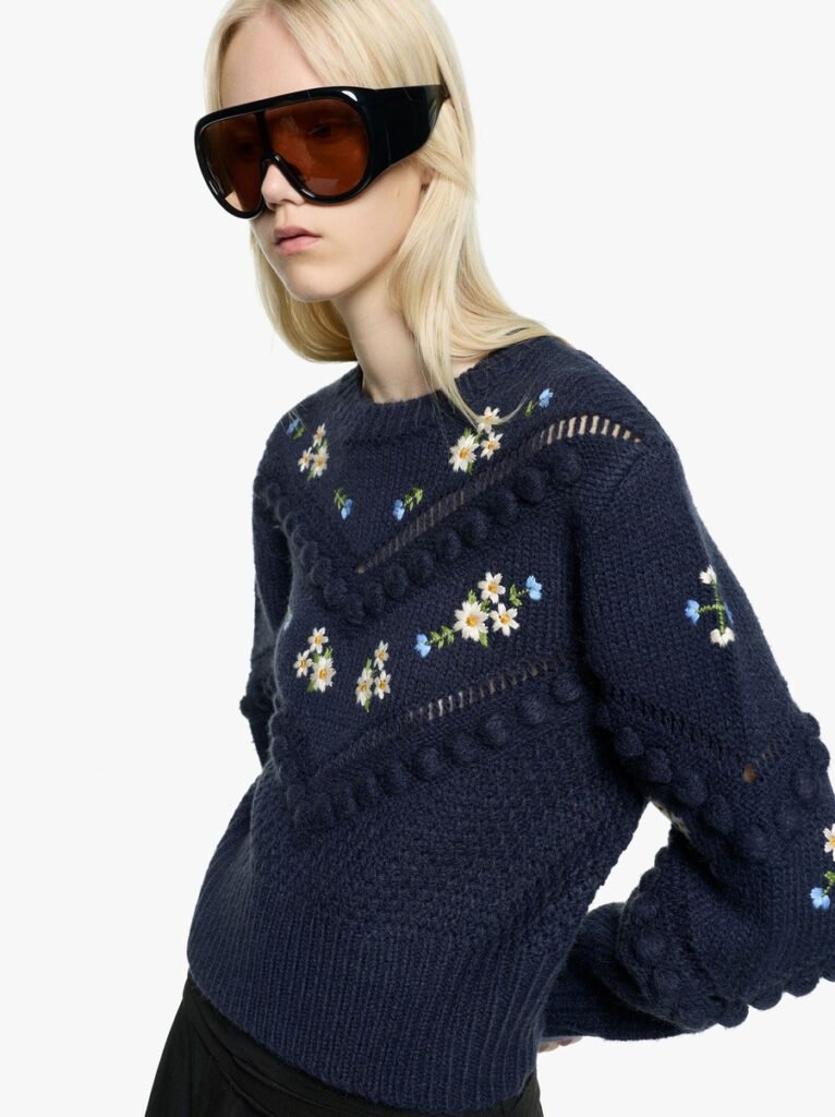 Modella con maglia blu a motivi floreali e occhiali oversize neri con lenti ambrate, nelle immagini Parfois The Edition.