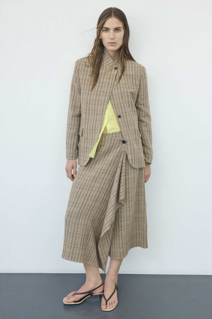 Modella con giacca e gonna asimmetrica a piccoli quadri Pomandère, top lime e sandali infradito.