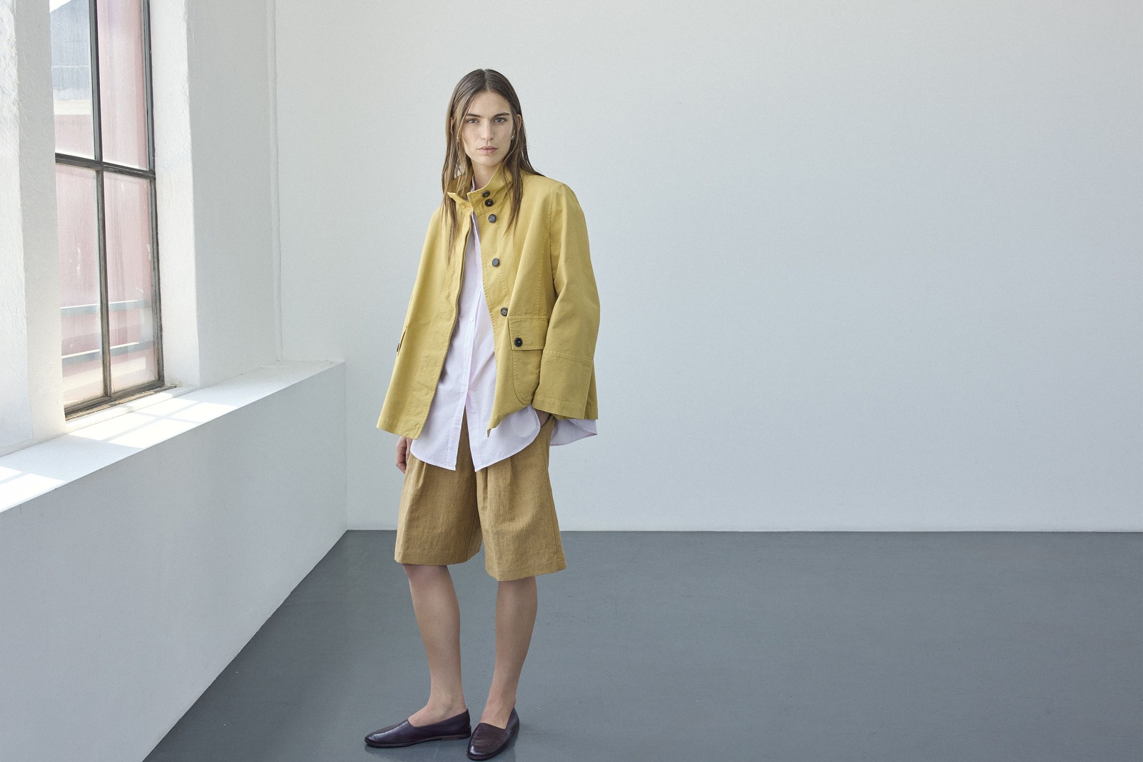 Modella con giacca gialla, camicia bianca lunga e bermuda color ocra della collezione Pomandère Sea Salt.