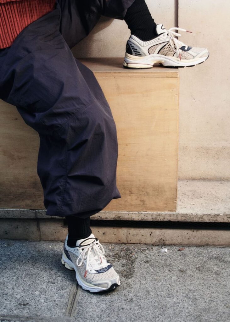 Sneakers Saucony x Highsnobiety ProGrid Paramount color crema, indossate con pantaloni ampi scuri e calze nere.