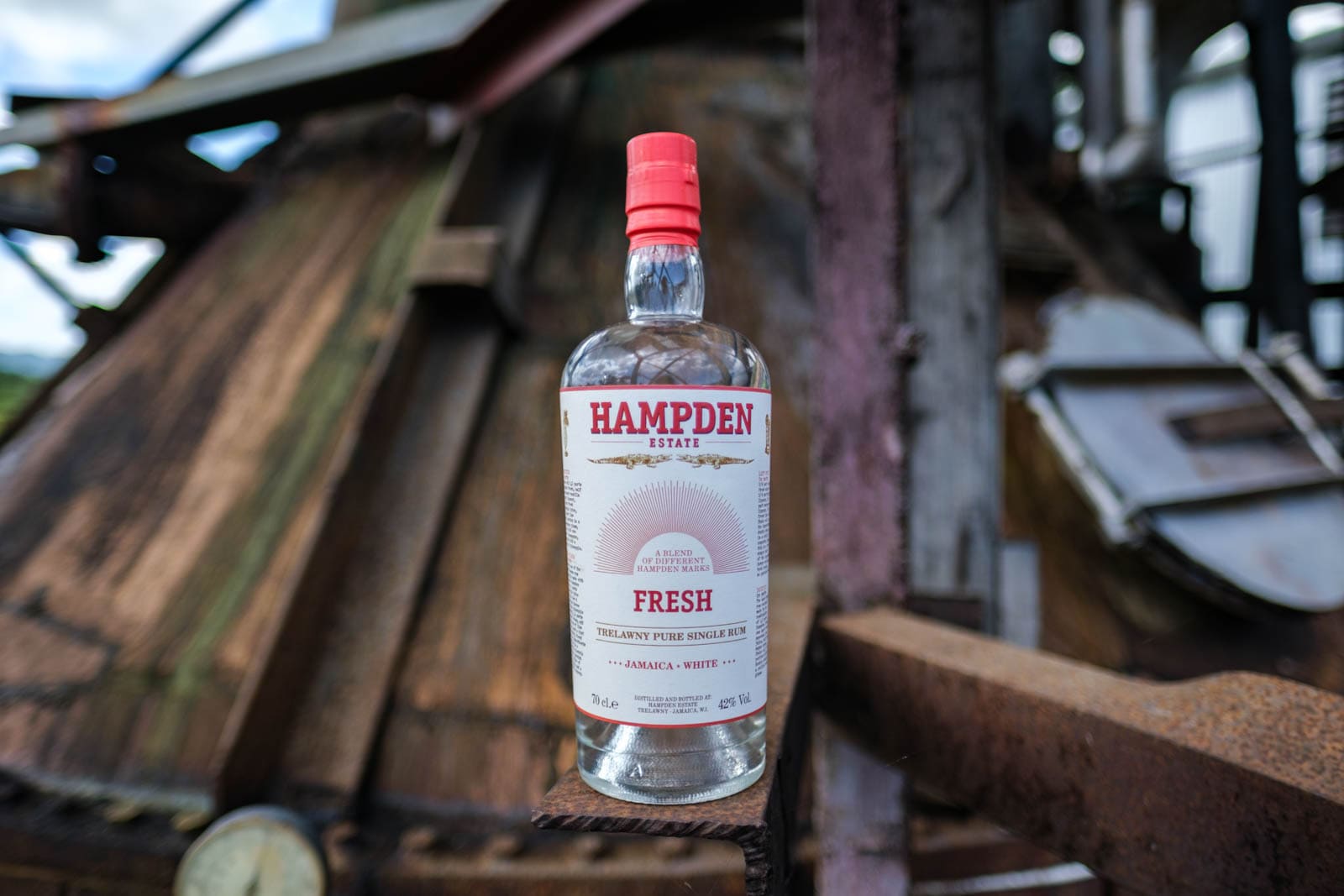 Bottiglia di rum bianco Hampden Fresh con tappo rosso, davanti a strutture in legno e metallo.