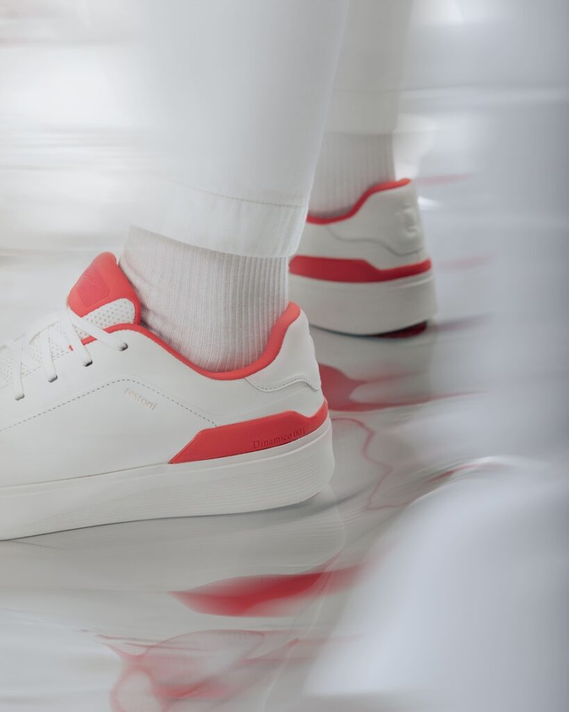 Sneakers Testoni Dinamico 001 bianche con lacci e dettagli rossi su linguetta, bordo e tallone, indossate con pantaloni chiari.